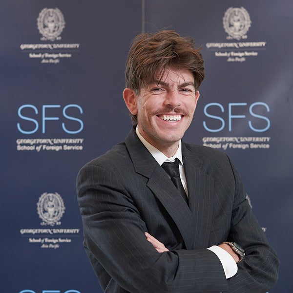 Headshot of Conor McWeeney wearing a suit, standing in front of a Georgetown SFS wall.