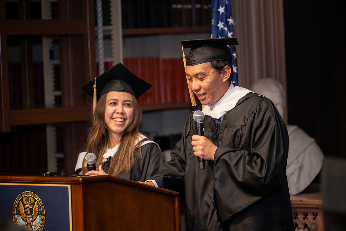Students in graduation gowns presenting on stage