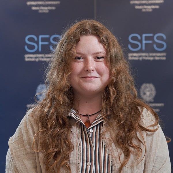 Kristen Bryant wearing a striped shirt, standing in front of a Georgetown SFS wall.