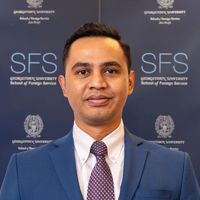 Portrait of Mega Puspita in a suit standing in front of an SFS backdrop.
