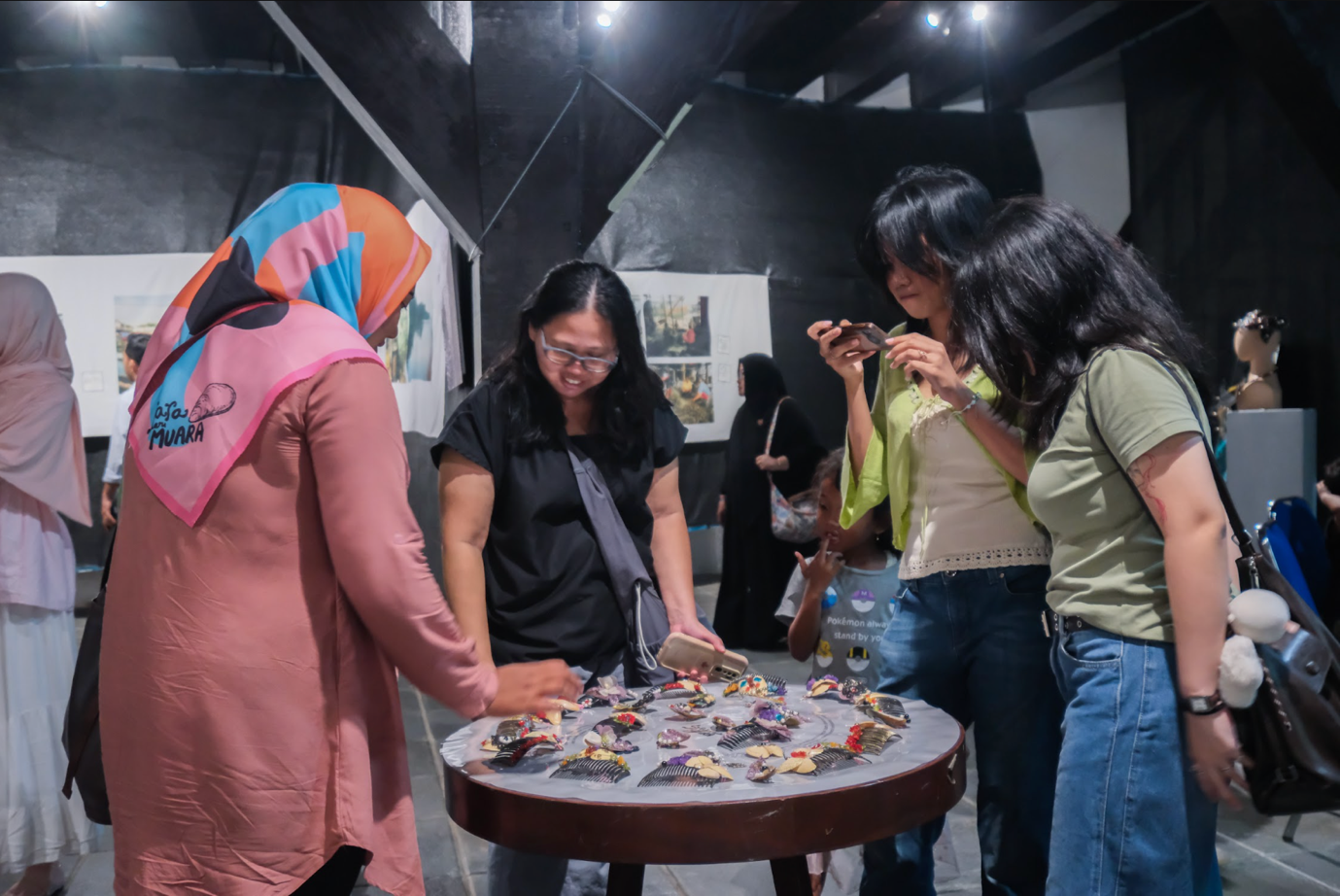 Visitors gather around a display table of handmade crafts while interacting with one of the Women of Muara Angke.